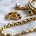 Collection of gold rings, bracelets, and chains with gemstones on a textured surface.